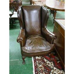 Leather upholstered wing armchair with carved front legs on lion paw tips.