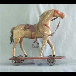 Wooden horse pull toy. Horse is mounted on a platform with iron  wheels. Original leather strappings