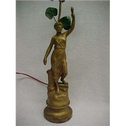 Gilt metal figural lamp of woman holding torch, one foot on books