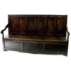 AN 18TH CENTURY OAK SETTLE of good colour, the crest rail carved fruiting vines, the six panel back.