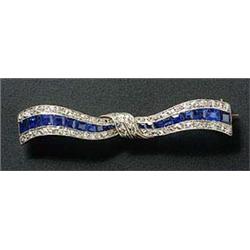 An Art Deco sapphire and diamond bow brooch, with a central calibre sapphire tapering band, flanked.