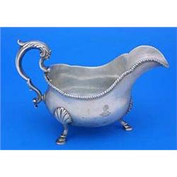 An early George III sauce boat with gadrooned border, leaf capped double scroll handle on shell and.