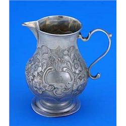 A George II small baluster shaped cream jug, with scroll handle, later embossed with flowers and lea