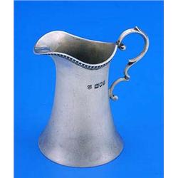 A small cream jug of waisted cylindrical form with a nulled border and scroll handle, London 1904 by