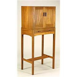 A 'Cotswold School' teak cabinet on stand, the plain top and sides having twin doors with carved bar