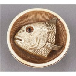 An ivory netsuke of a fish head in a bowl.