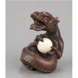 A wood netsuke of a roaring dragon holding a ball.