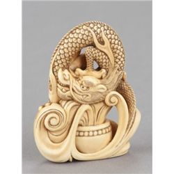An ivory netsuke of a dragon emerging from an alms