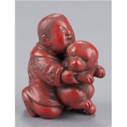 A carved tsuishu netsuke of a boy with puppy.
