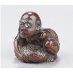 A wood netsuke of a blind man lifting scrotum.