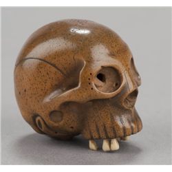 A wood netsuke of a skull with ivory teeth.