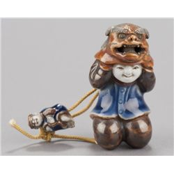 A Hirado-ware netsuke of a boy with Shishi mask.