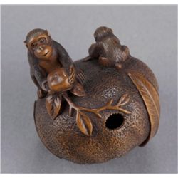 A wood netsuke of monkeys on an orange.