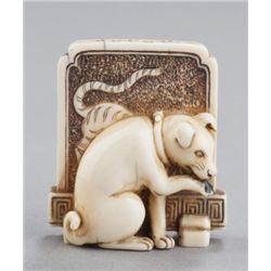 An ivory netsuke of dog seated in front of tsuitat