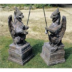A pair of terracotta gate pier finials in the form of crouching gryphons bearing iron spears, on squ