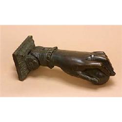 A patinated bronze door knocker in the form of a hand, the rectangular top with a stiff leaf border,