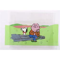 A Peanuts animation cell depicting Charlie Brown and Snoopy, with Charlie seated on a log and Snoopy