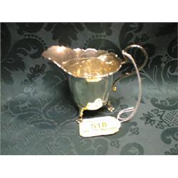 A silver cream jug having a folded shaped rim, scroll handle and on 3  claw feet.  Birmingham 193