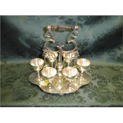 An Edwardian EPNS egg stand, the shaped base supporting 6 egg cups,  with centre scroll handle wi