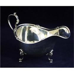 A SILVER SAUCE BOAT: with tube lined and decorated rim with scroll  handle, raised three scroll a...