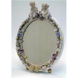 A 19th century Dresden porcelain oval dressing mirror, encrusted with foliage and twin cherub cre...