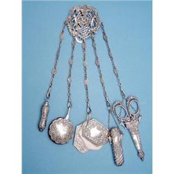 A late Victorian silver chatelaine fitted with pencil, pin cushion, note case, needlecase and sci...