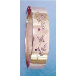 A gold diamond and ruby set hinged bangle, the front decorated with a swallow on a flowering bran...