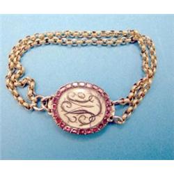 A Georgian gold oval bracelet clasp with hair work monogram framed by a border of flat cut garnet...