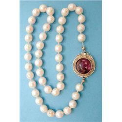 A single row uniform cultured pearl necklace with circular gold clasp set with a cabochon amethys...