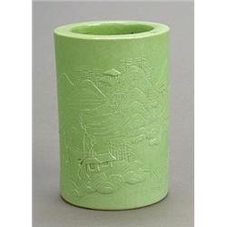 A green-glazed brushpot, circa 1900, carved in low relief with a landscape, the base with four ch...