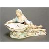 A Meissen figural table salt modelled as a recumbent women holding a shaped bowl, the interior pa...