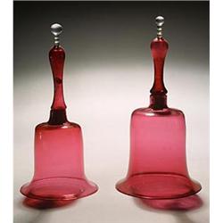 Two cranberry models of hand bells, each with a hollow handle and clear finial, 28cm & 29cm high,...
