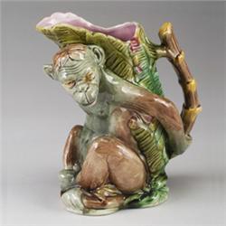 ENGLISH MAJOLICA monkey jug, circa 1880, modeled as a seated monkey holding a stalk of bamboo, pi…