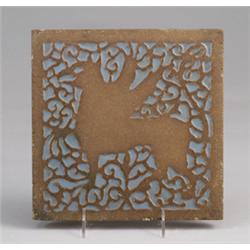 ROOKWOOD Faience tile depicting a winged griffin in brown clay against a blue-gray glazed ground.…