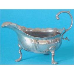 A George II silver sauceboat, with shaped rim and upscrolled leaf capped handle on three C scroll...
