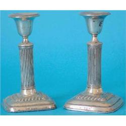 An Edwardian pair of silver dwarf candlesticks with vase shaped nozzles, reeded stems and square...