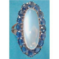 A gold dress ring claw set with a long oval moonstone within a border of 16 cushion shaped sapphi...
