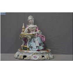 A vintage Dresden figurine of a figure in Rococo dress seated at a table reading complete with hand 