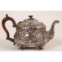 A George III Silver Teapot, crested, with flower finial, the body chased scrolling foliage, and w...