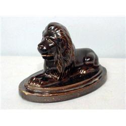 WHITE CLAY LION. Alert lion reclining on an oval base. Dark brown, shiny glaze. Incised initials.…