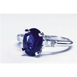 PLATINUM RING, set with a fine oval cut sapphire (approx. 2.50ct.) flanked by 2 small tapered bag...