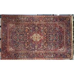 A KASHAN RUG, c.1920, the blue floral field with a red pendant medallion enclosed by red spandrel...