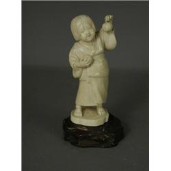 A late 19th century Meiji period carved ivory okimono of a young girl holding aloft an apple, thr...