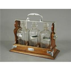An Edwardian three bottle tantalus, each with plated decanter labels; brandy, sherry and whiskey,...