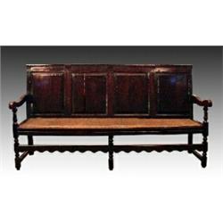 A mid 18th Century oak settle, the four panelled back and scrolled armrests above a leather studd