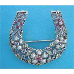 A gold openwork horseshoe shaped brooch, set rubies, sapphires, demantoid garnets and split pearl...