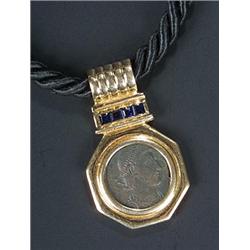 A modern 18ct gold, sapphire and coin pendant on a black silk necklace, the bronzed coin within a...