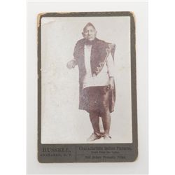 Photograph of Native American weaving a rug in  tribal dress.  An original card, reads "Russell  Ana