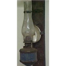 Oil lamp with brass font in painted metal holder, mounted on wood panel, with mercury glass refle...