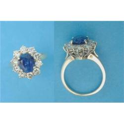 An 18ct gold cluster ring, claw-set with an oval sapphire in a border of 10 brilliant cut diamond...